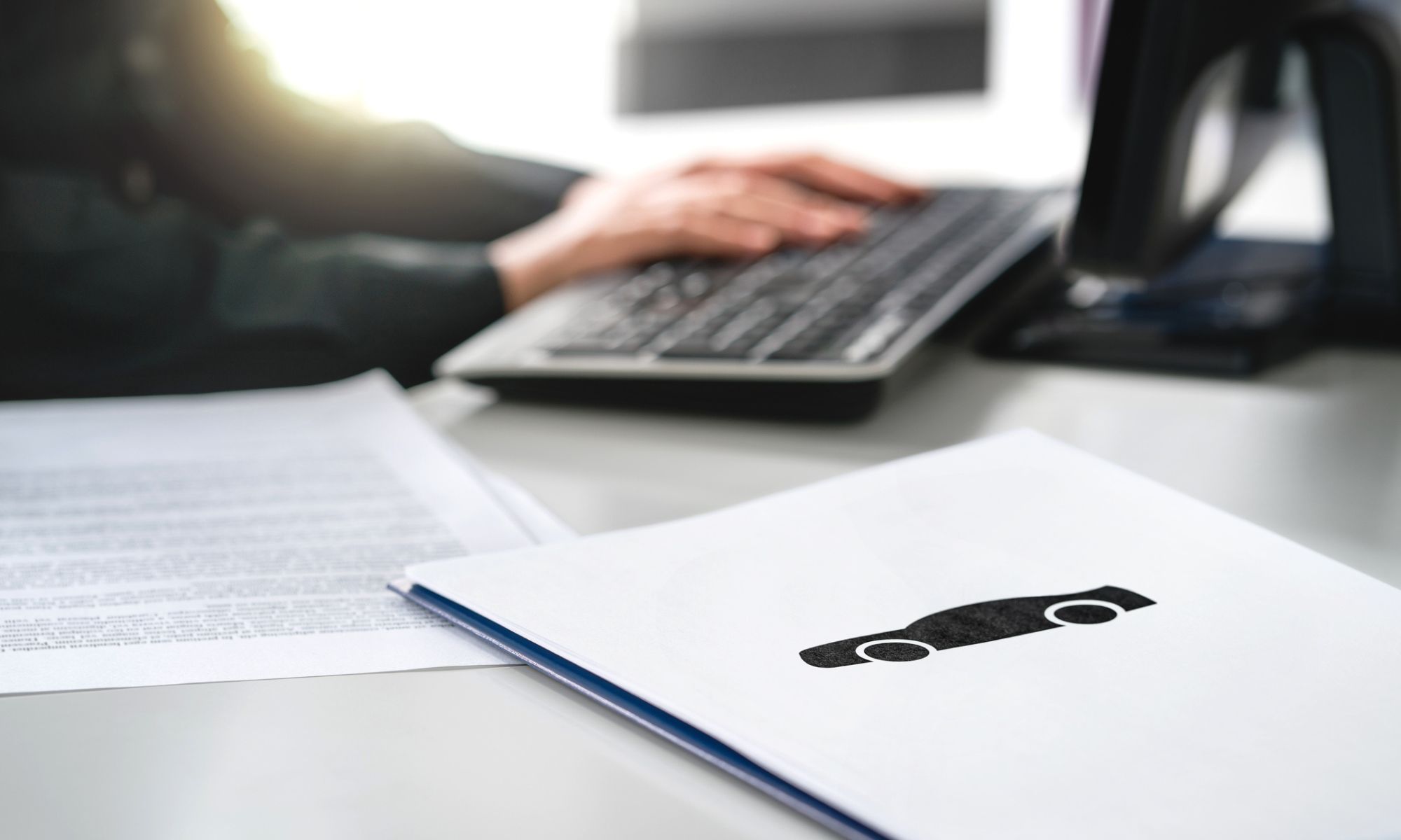 Car paperwork on a desk with a computer