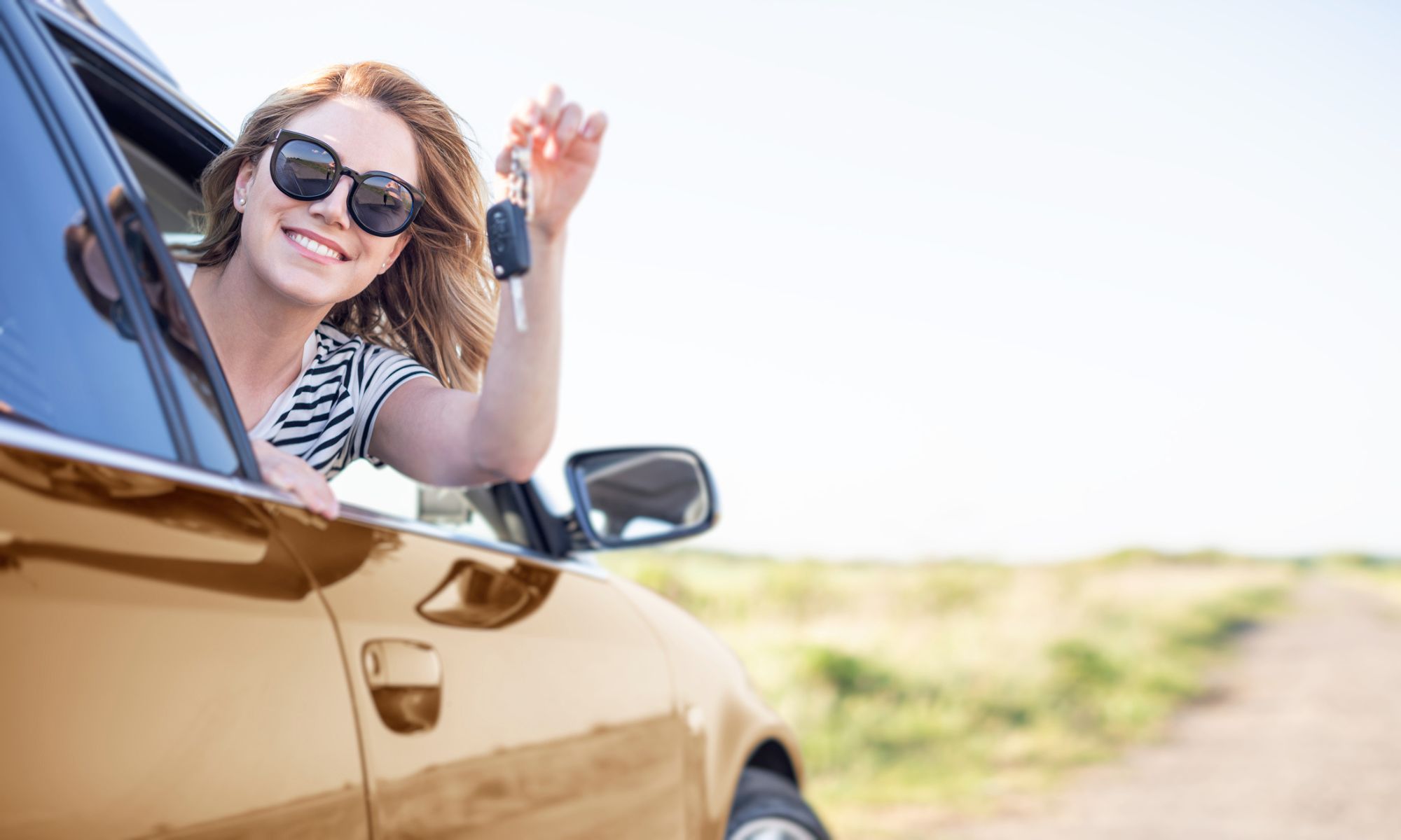 Woman in sunglasses holding up a key to her Honda car