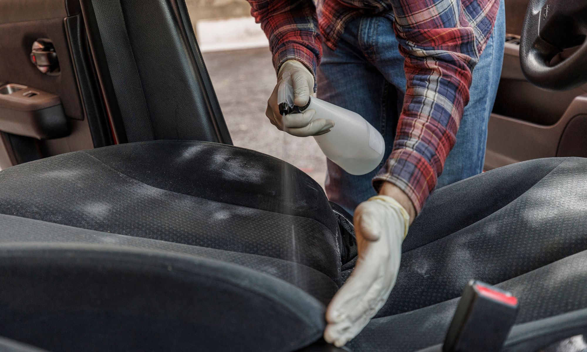 A man spraying driver's seat with special detergents to remove stains