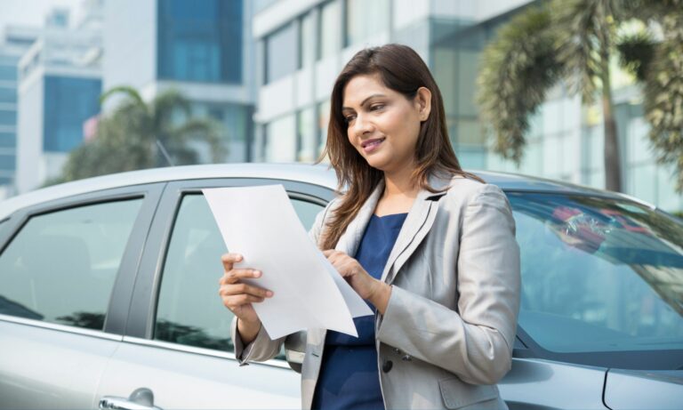 Woman in suit jacket reading a car valuation in front of her vehicle