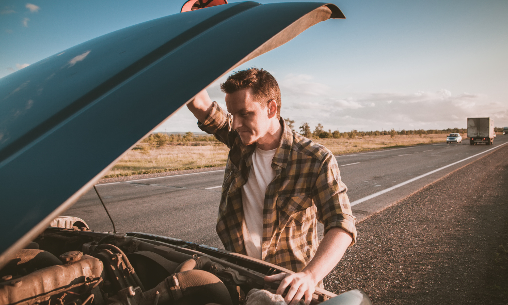 Man looking at the engine of his broken down car on a California highway