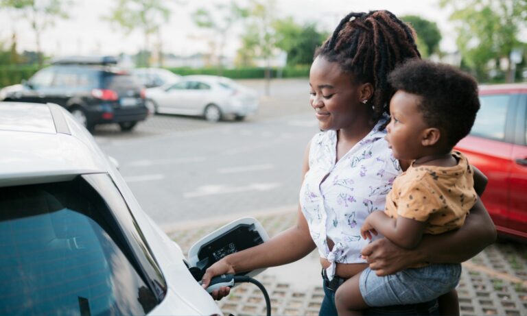 Mother charging her electric car parked next to the charging station while holding her baby