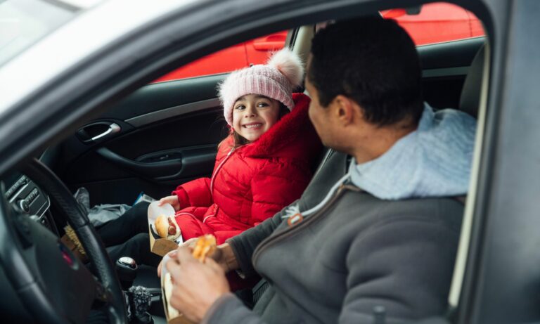 Father and daughter eating hot dogs together sitting in their car