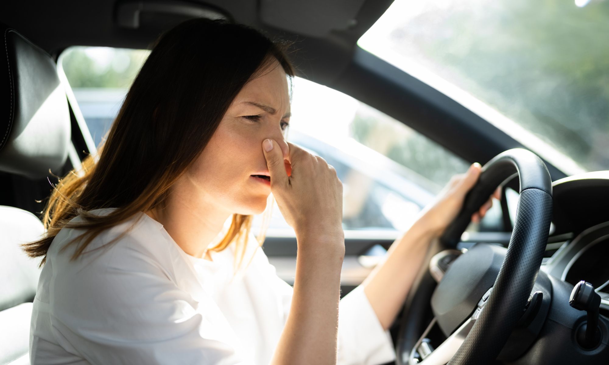 Woman in her car holding her nose because it smells bad