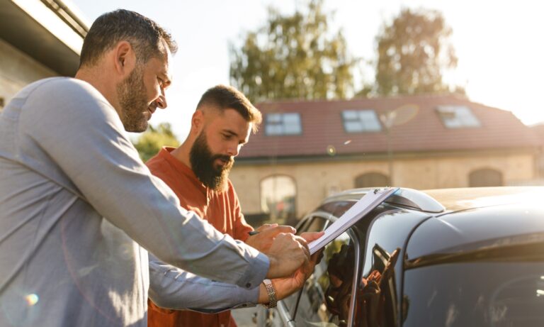 Two men looking at paperwork for an extended warranty in front of a used car