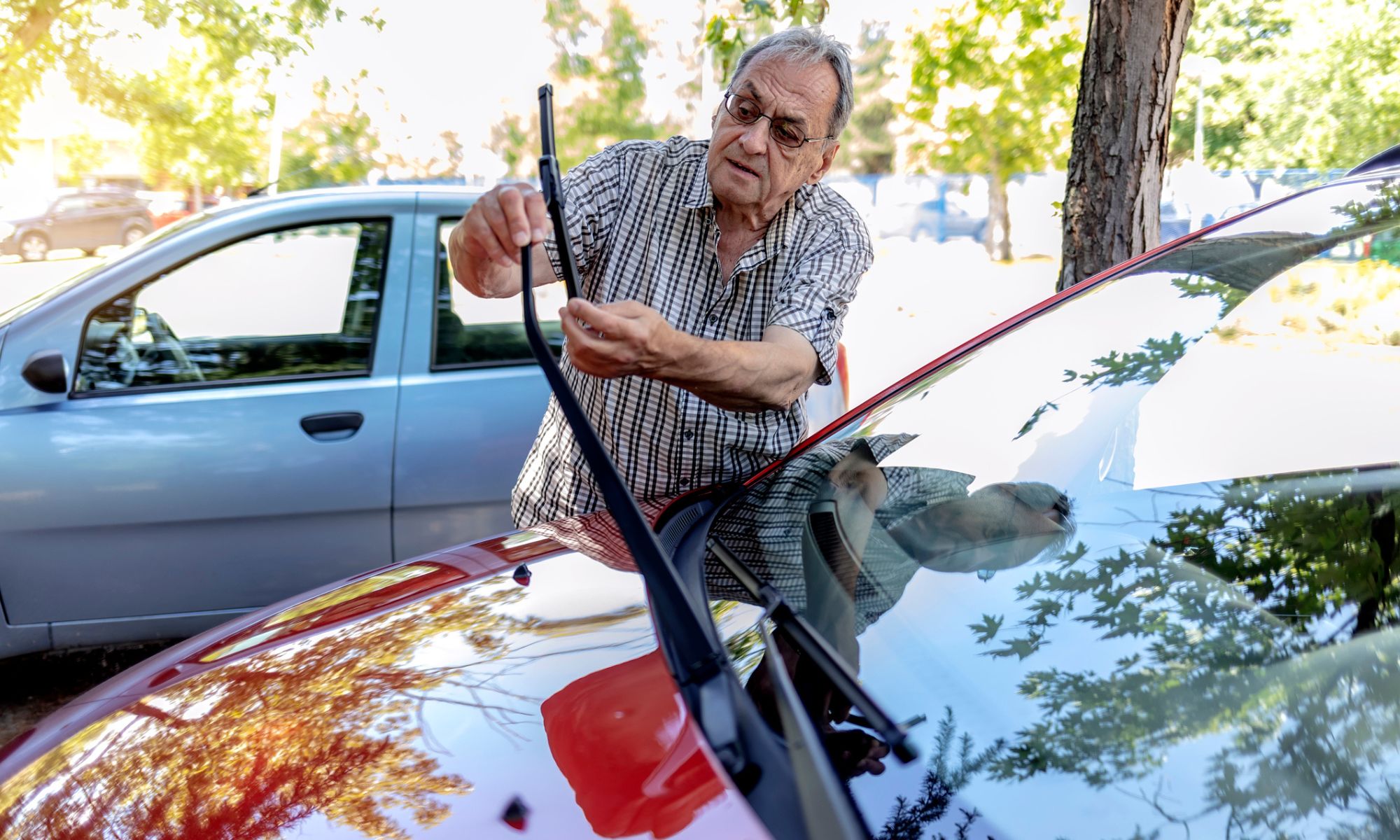 Elderly man with eyeglasses picking up windshield wiper and checking it