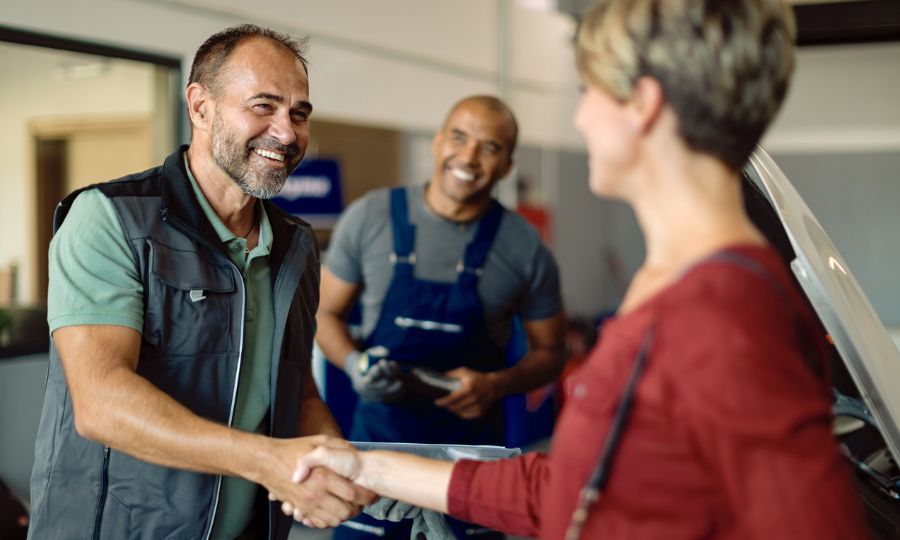 Happy car mechanic and his customer shaking hands while greeting in auto repair shop