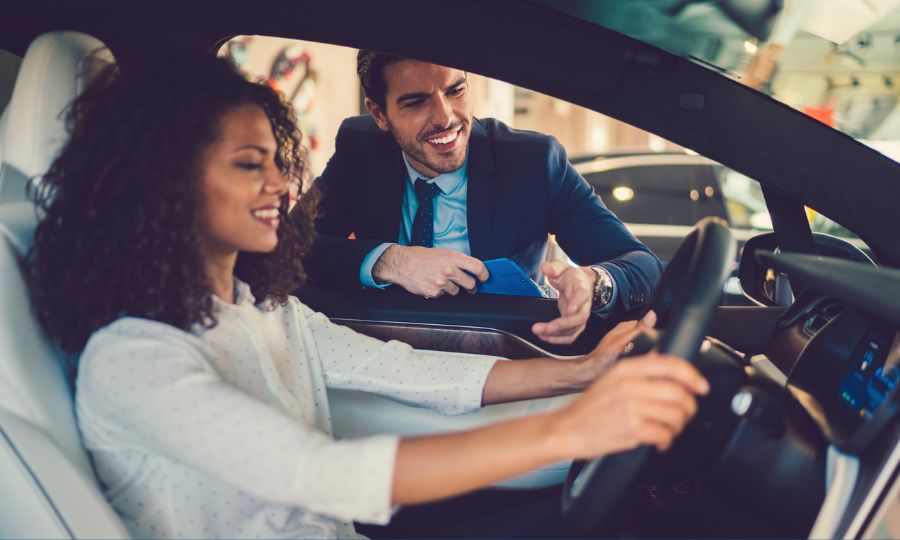 Smiling woman in the showroom enjoying luxury car talking to a car salesman