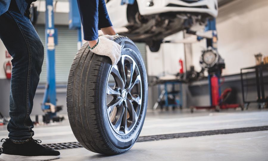 Male mechanic hold and rolling tire at repairing service garage background