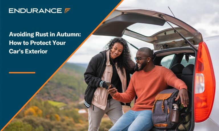 Man sitting and woman standing by the back of their car with an autumn backdrop