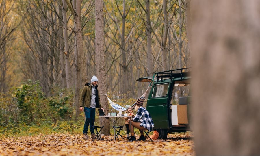 Family drinking coffee and tea while sitting outside their van in the forest