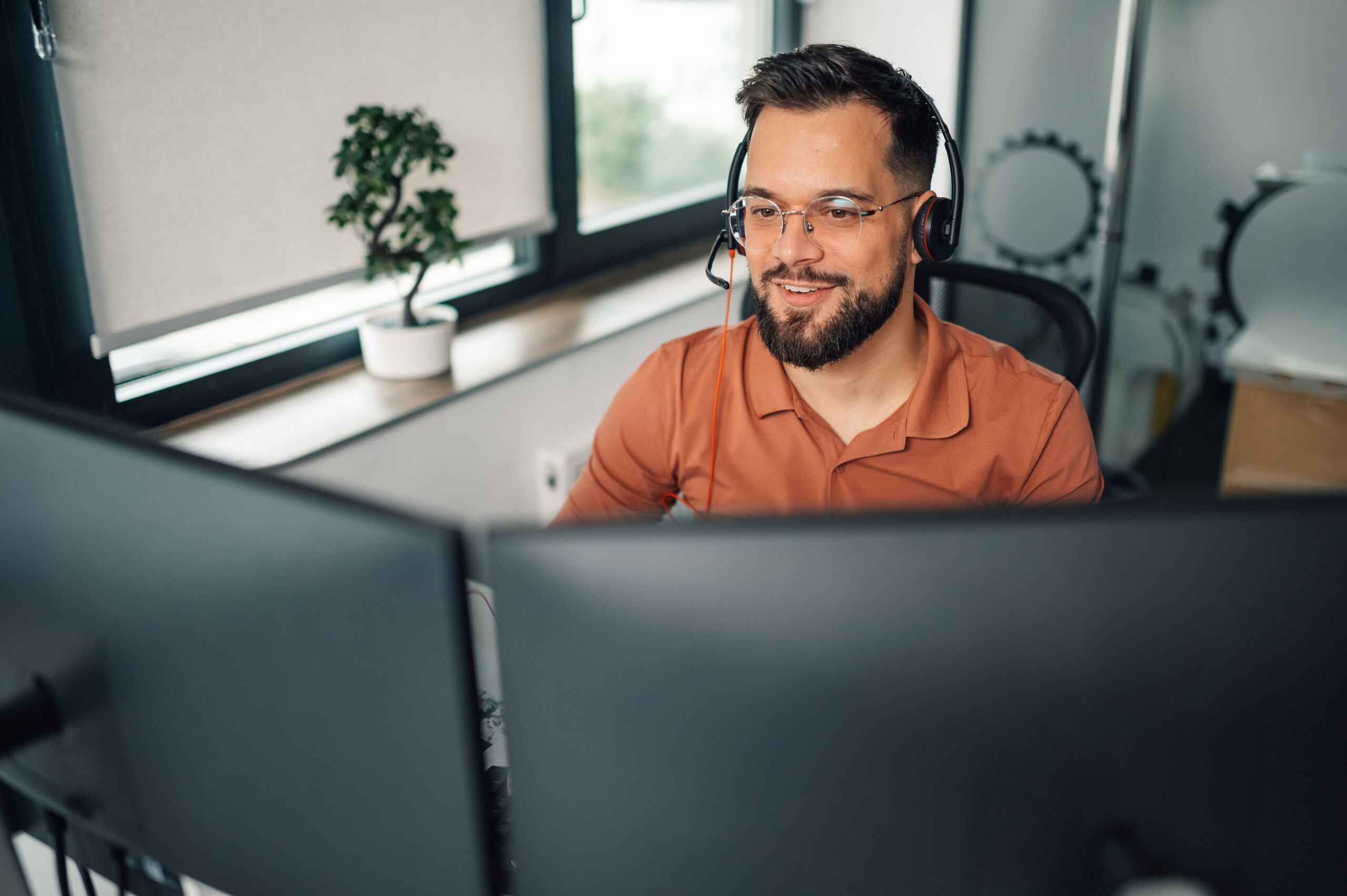 Hombre de negocios trabajando desde su oficina moderna, usando auriculares y una computadora de doble pantalla, concentrado en su trabajo, brindando soporte en línea a los clientes.