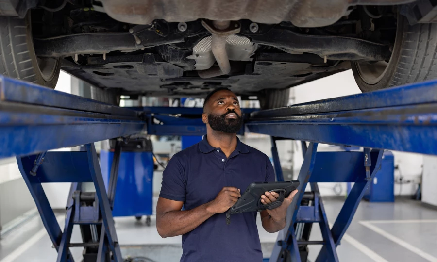 Mechanic looking at a car's chassis while holding a tablet in a repair shop