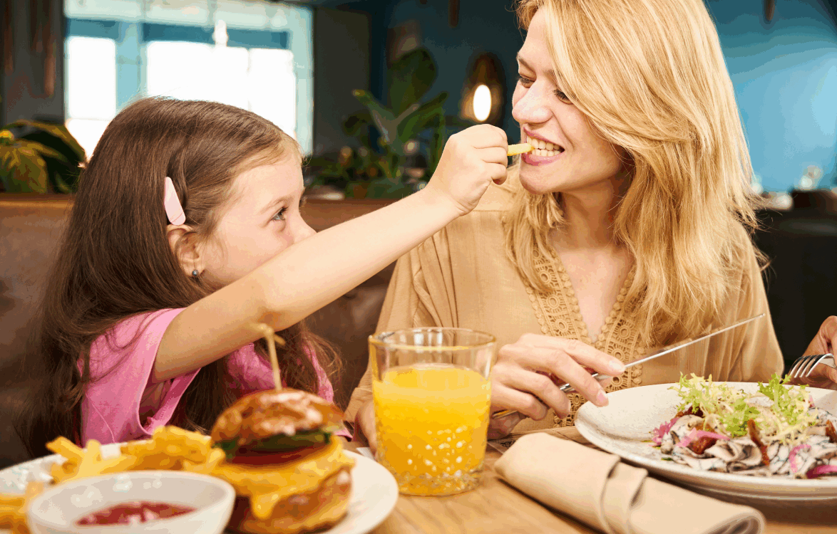 Girl in restaurant sharing a french fry with her mother