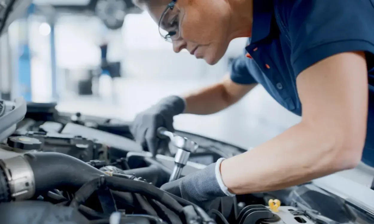 Female mechanic working inside of the hood of a car