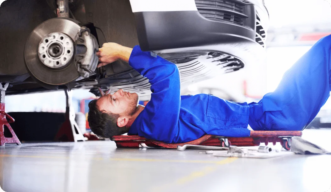 Mecánico varón con uniforme azul trabajando debajo de un coche blanco