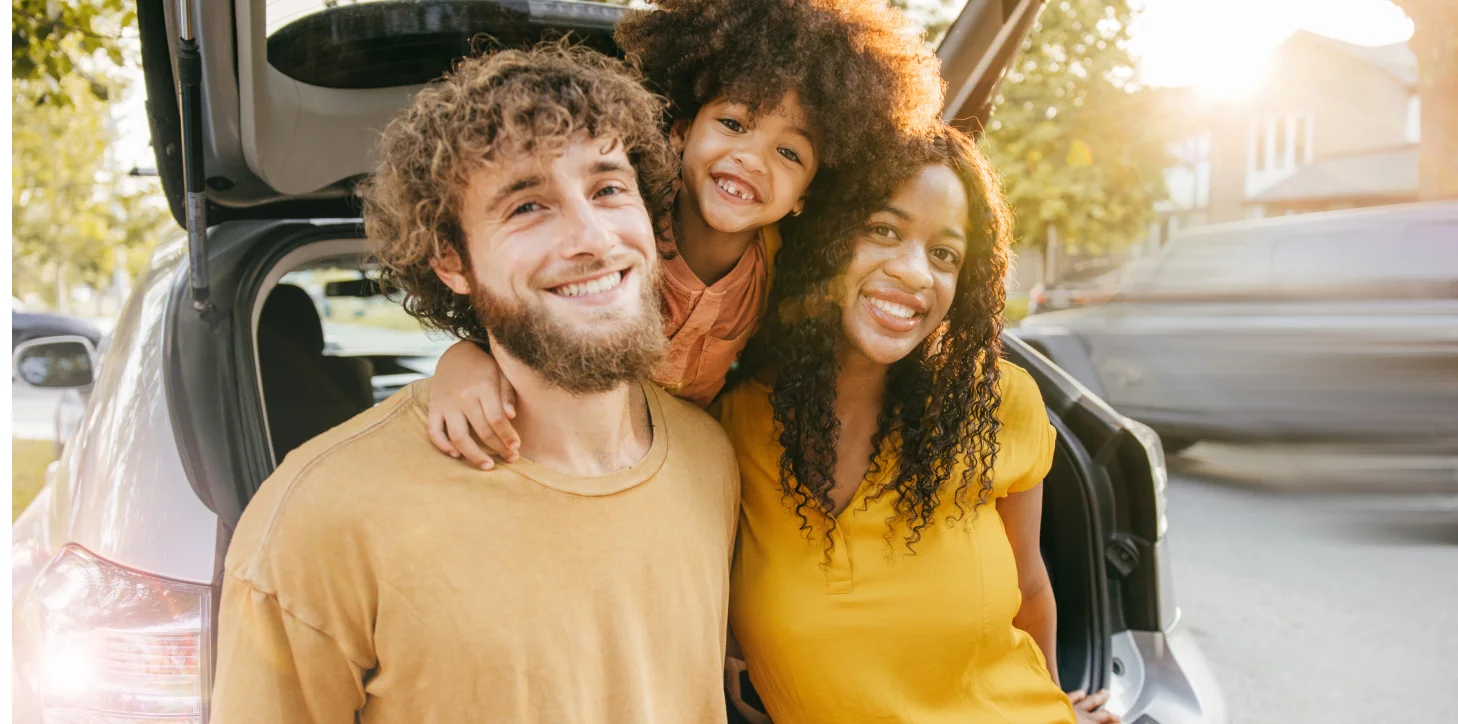 Familia sonriente de pie detrás de una camioneta SUV
