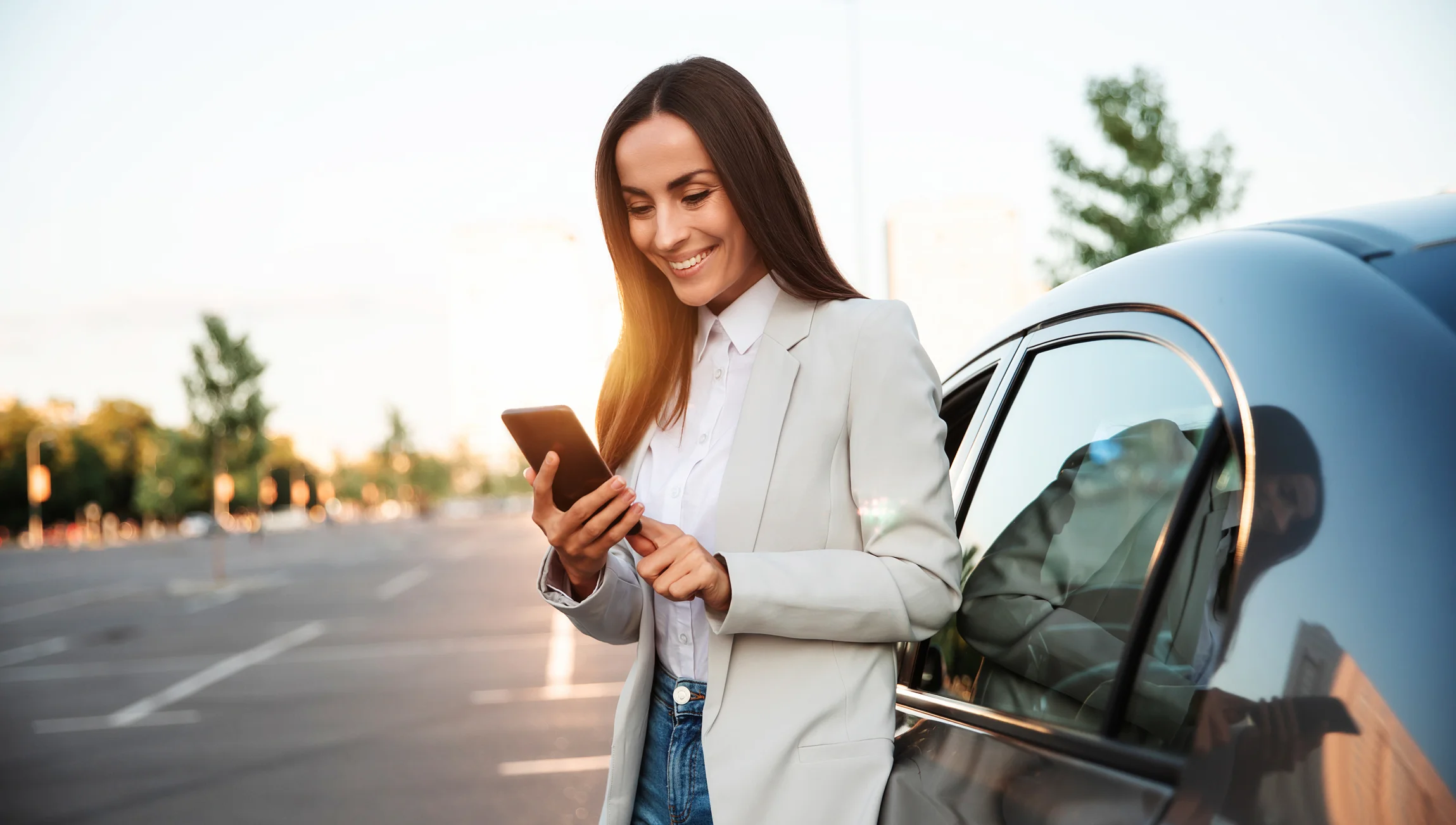 Woman Smiling At Phone While Standing By Her Car